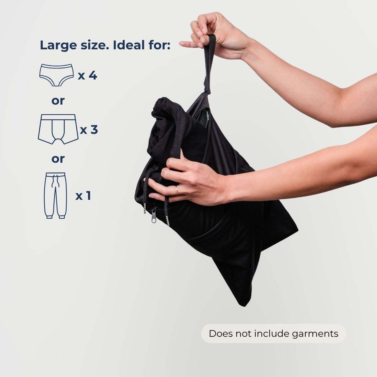 Black dual pocket drybag held by hands with text indicating its size suitability for clothing items on a light gray background.
