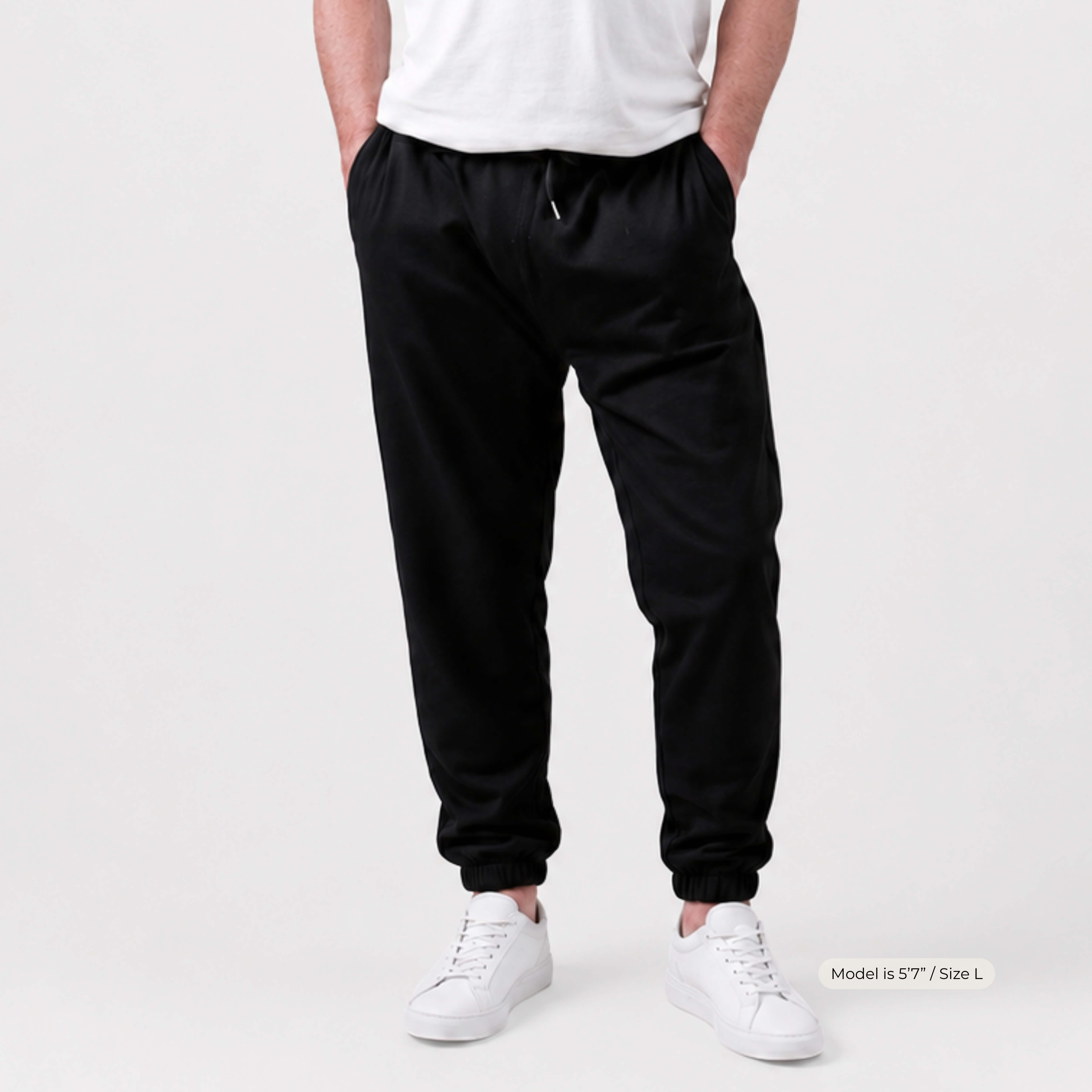Man wearing Kovered leakproof black jogger pants and white sneakers on a plain background
