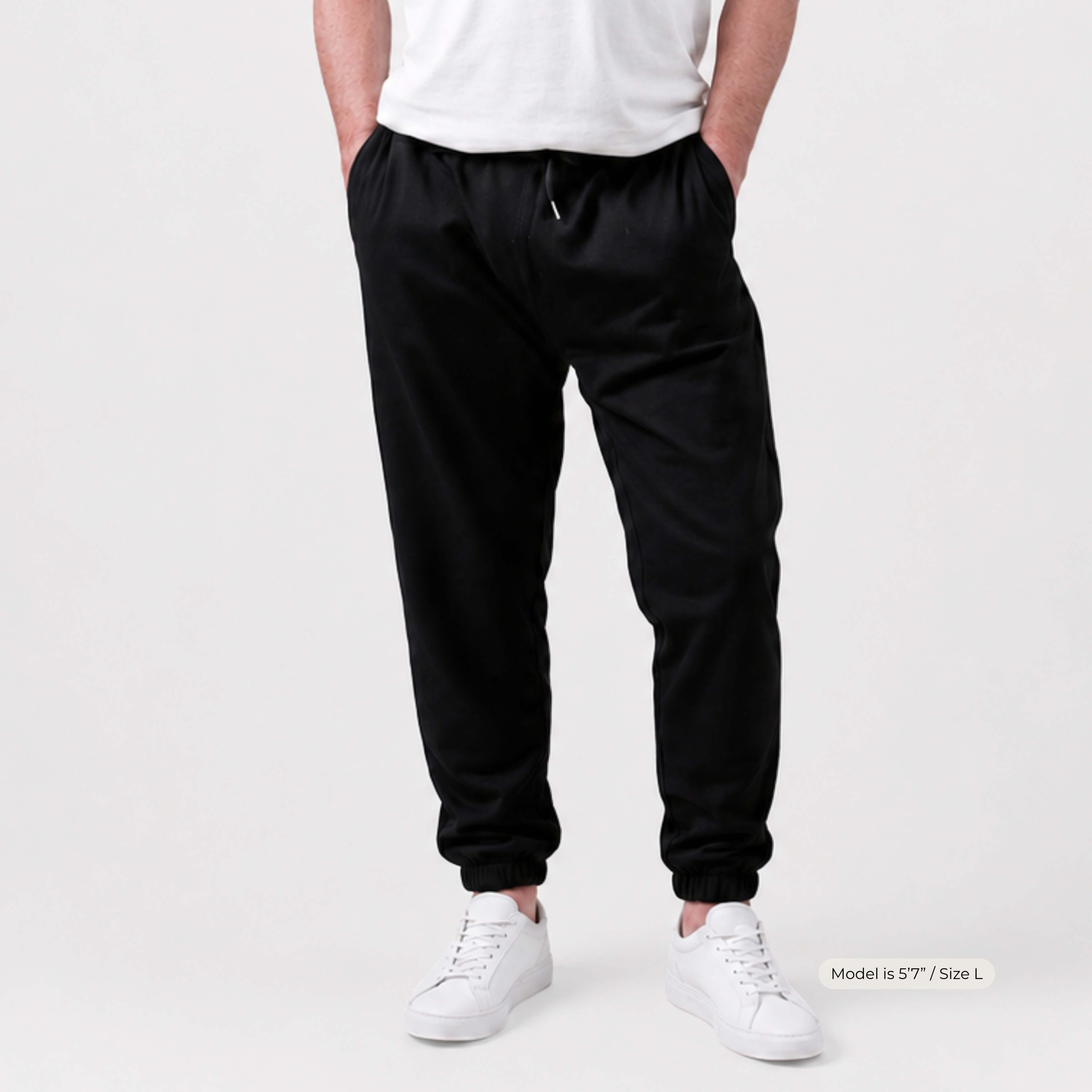 Man wearing Kovered leakproof black jogger pants and white sneakers on a plain background