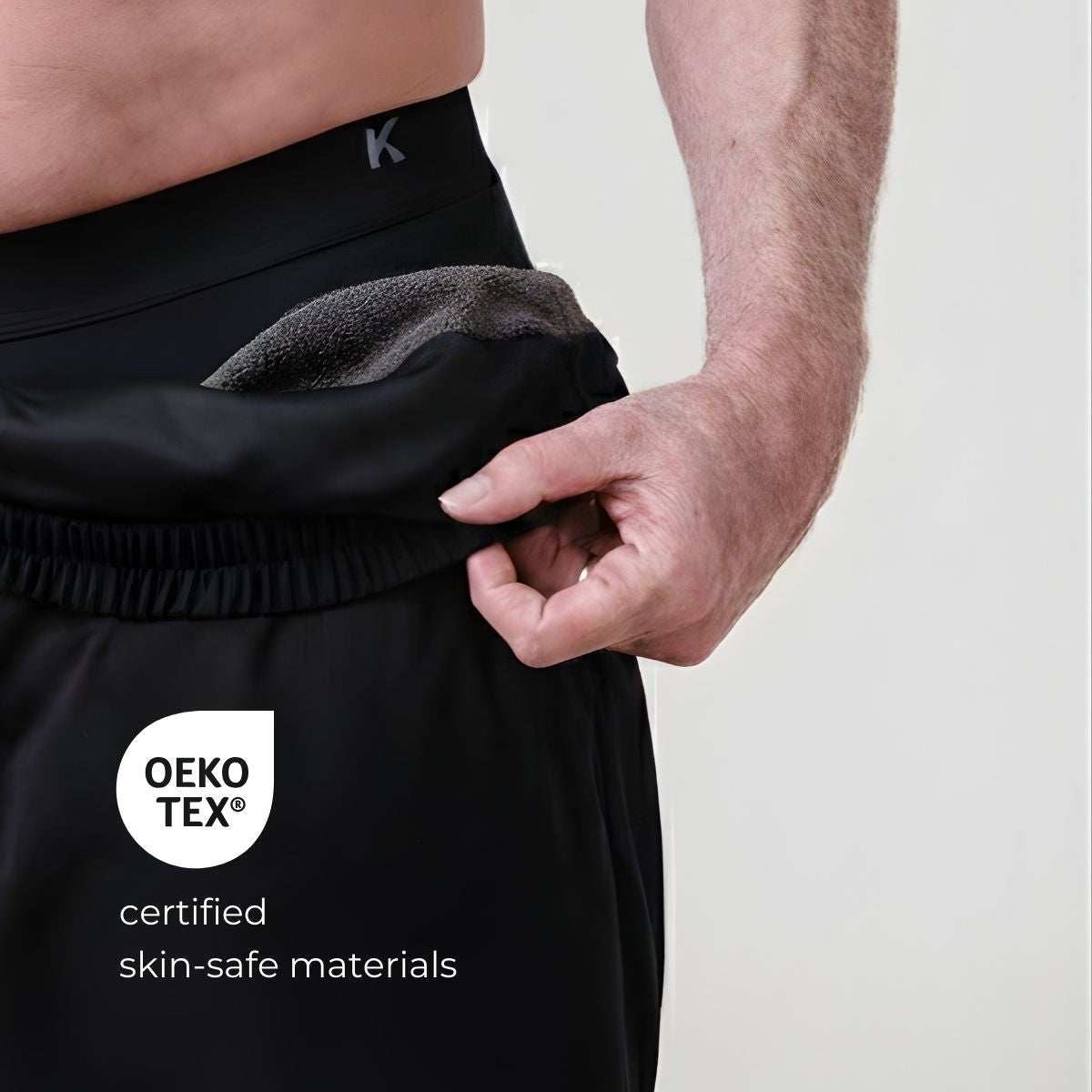 Person wearing kovered leakproof black pants with a visible brand logo and OEKO-TEX certification label on a light gray background.
